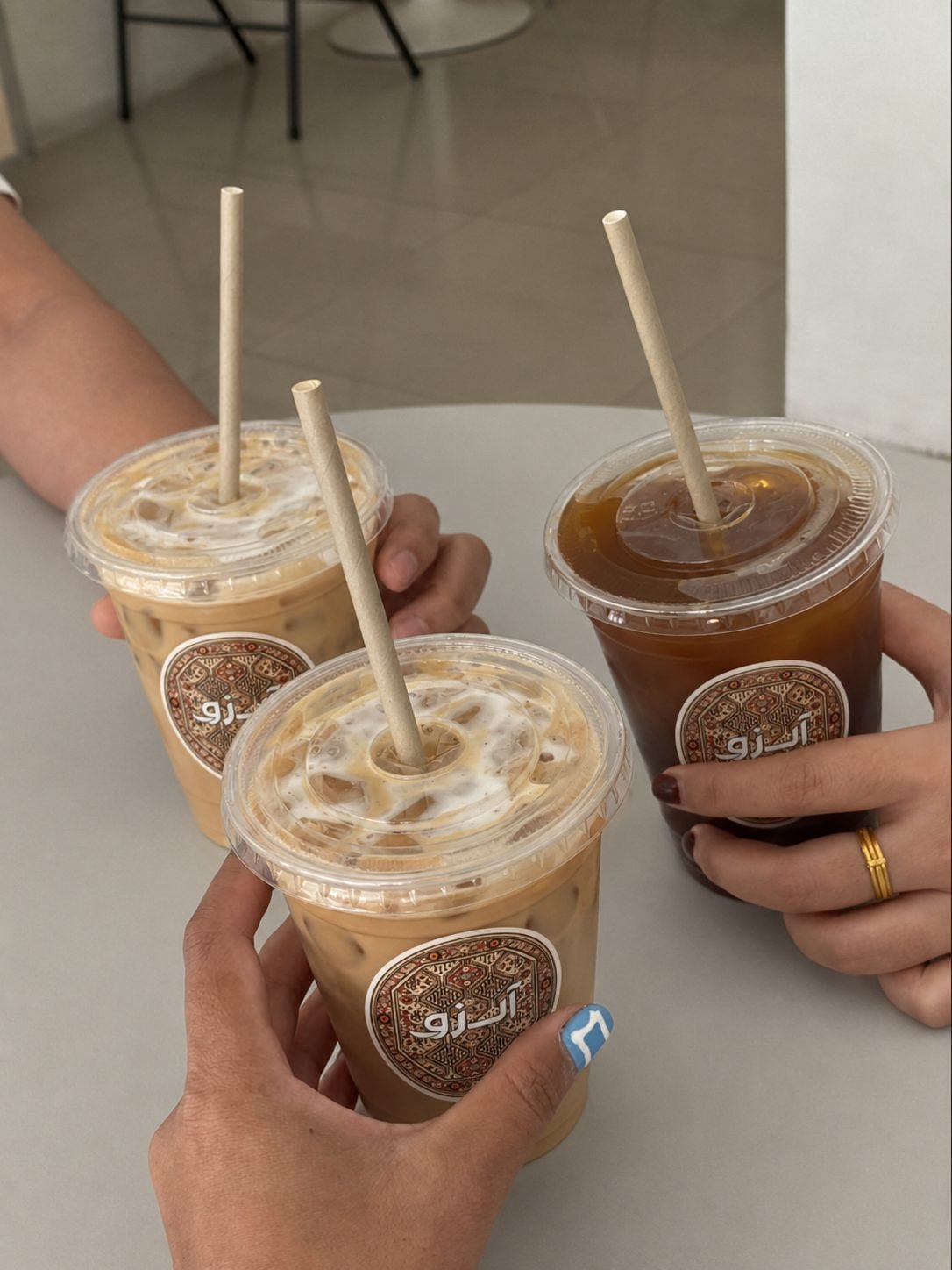 Three iced Arzu Coffee Co. drinks, each cup marked with the rug-medallion logo, held up together